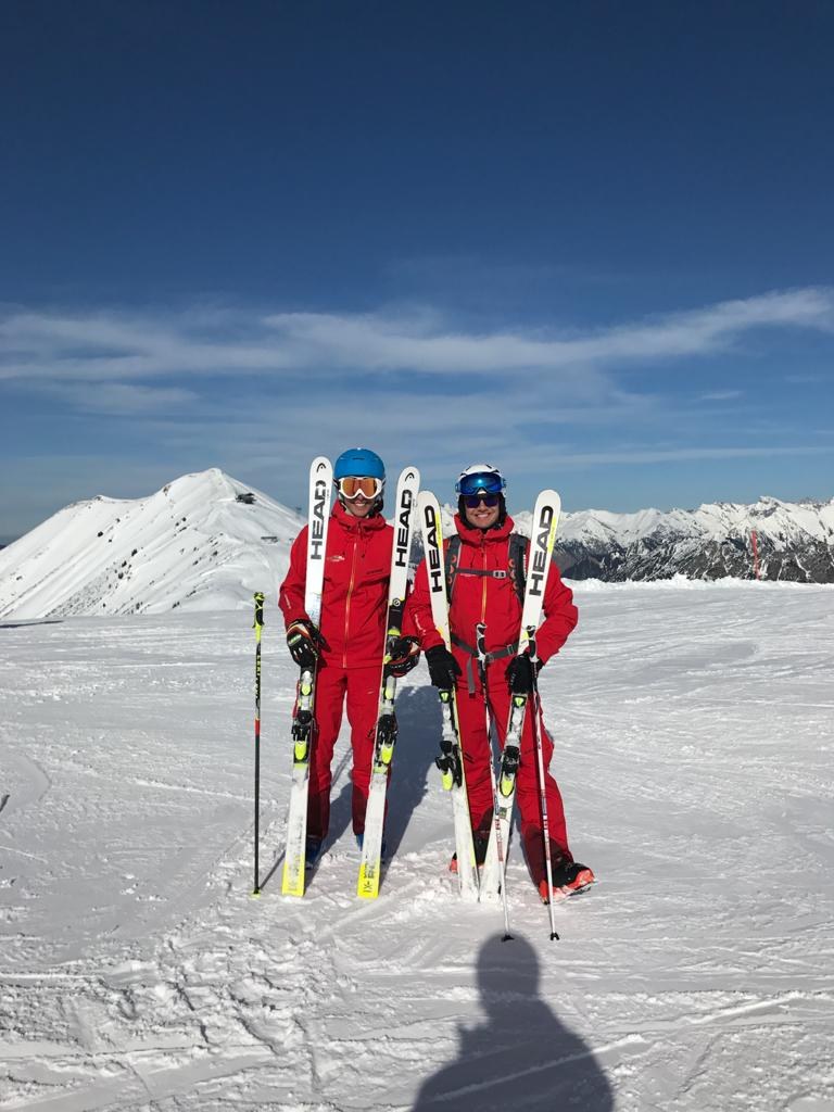 Zwei Skilehrer des Vereins in roten Anzügen auf einem Gipfel