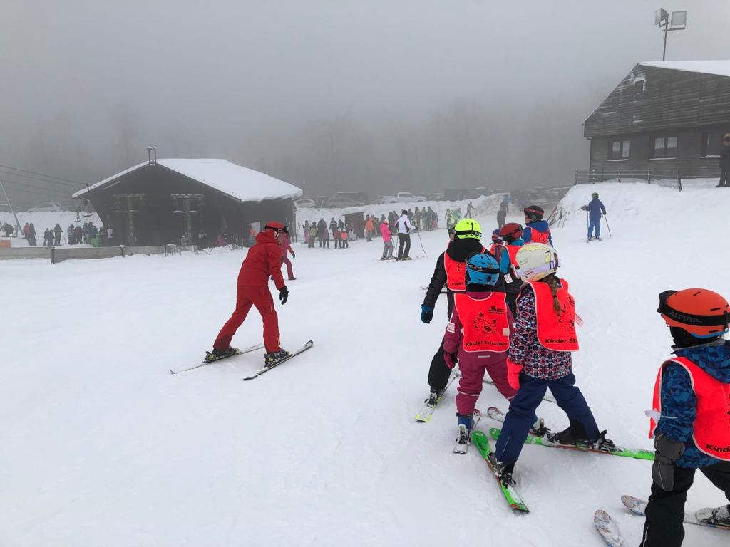 Kinder folgen einem Skilehrer während eines Skikurses